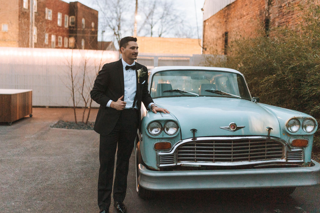 groom posing near a blue car