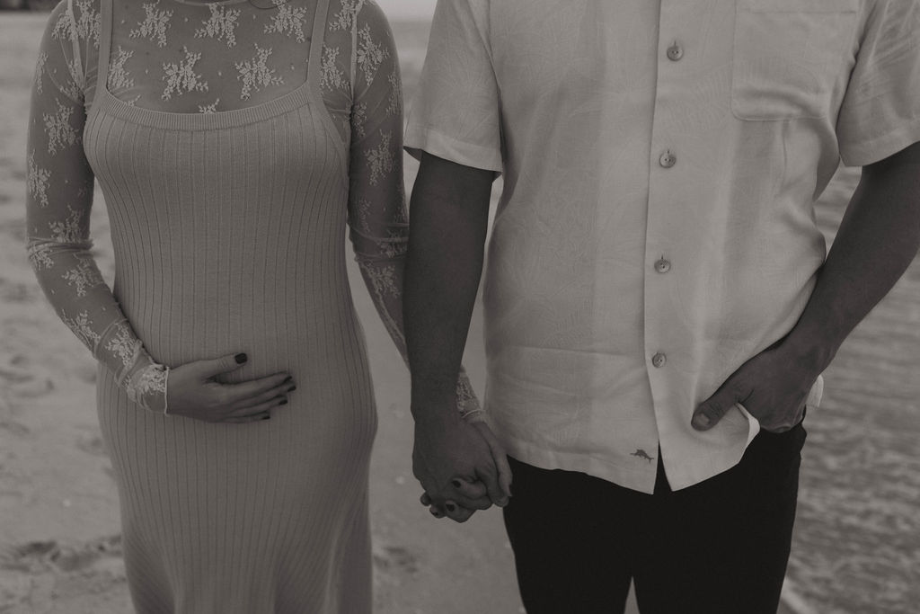 Couple holding hands during their baby announcement photoshoot at Naples Beach, FL