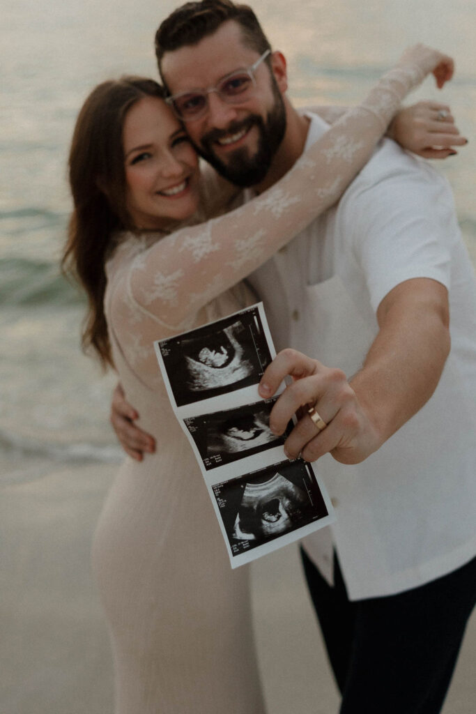 couple holding their ultrasound and smiling at the camera