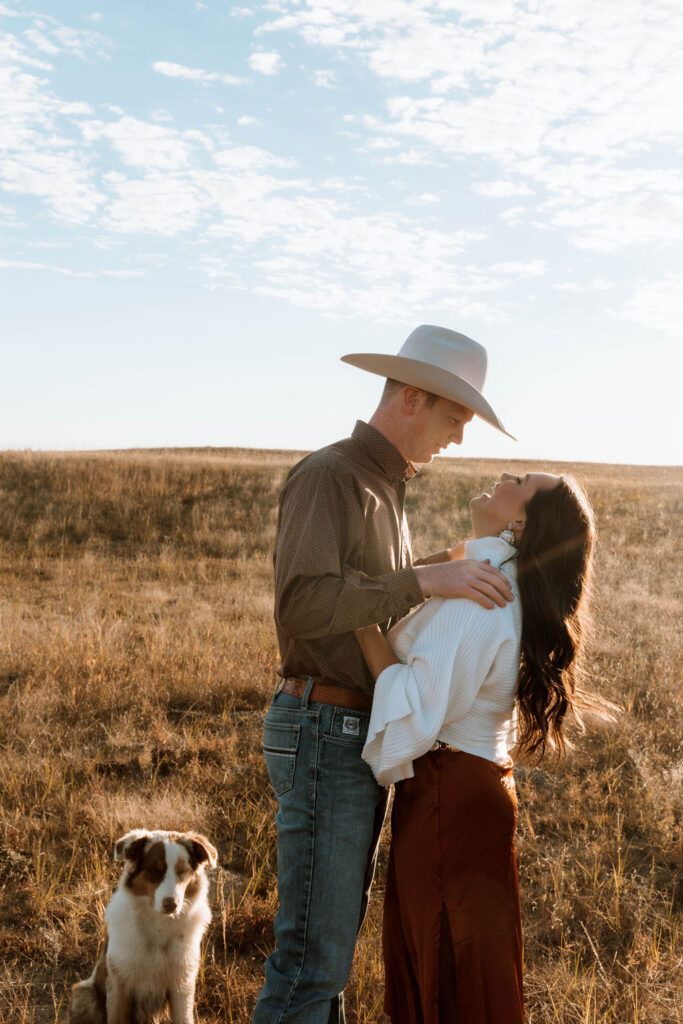 beautiful couple during their country session with the sunset and their dog in the background